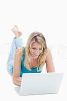 A smiling woman with a laptop is lying on the ground with her le
