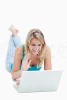 A woman with a laptop has her hand up and is lying on the floor