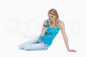 A smiling woman is sitting on the floor holding her mobile phone