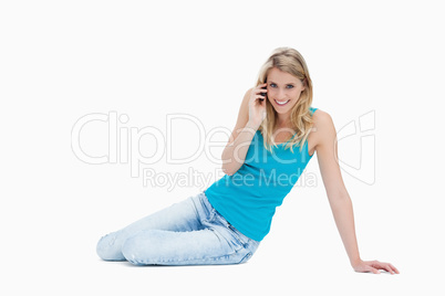 A smiling woman is sitting on the floor talking on her mobile ph
