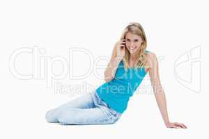 A smiling woman is sitting on the floor talking on her mobile ph