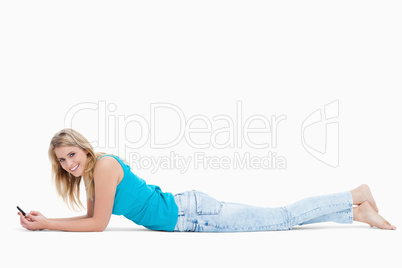 A smiling woman holding a mobile phone is lying on the floor