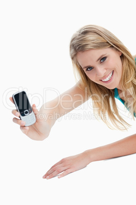 A young woman holding out her mobile phone is looking at the cam