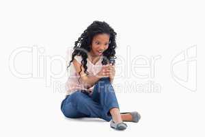 A surprised woman is sitting on her floor looking at her mobile
