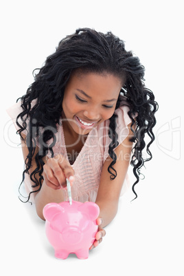 A young girl lying on the floor putting money into a piggy bank