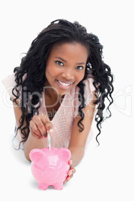 A young girl looking at the camera is putting money into a piggy