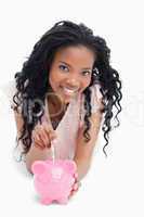 A young girl looking at the camera is putting money into a piggy