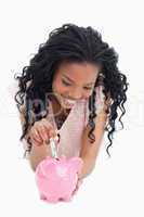 A young woman lying on the floor is putting money into a piggy b