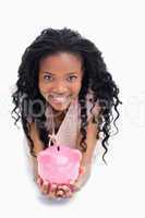 A young woman smiling at the camera is holding a piggy bank in h