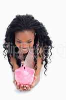 A smiling woman is looking at a piggy bank she is holding