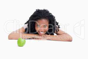 A smiling girl is resting her head on her hands with an apple in