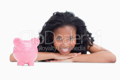 A smiling girl resting her head on her hands with a piggy bank i