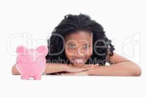 A smiling girl resting her head on her hands with a piggy bank i