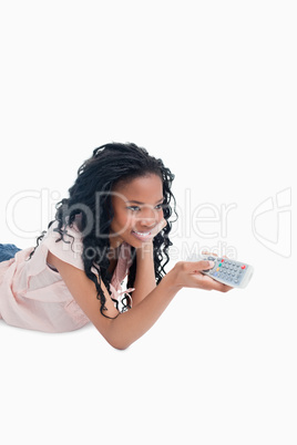 A young girl lying on the floor is holding a television remote c