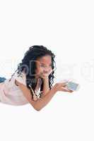 A young girl lying on the floor is holding a television remote c