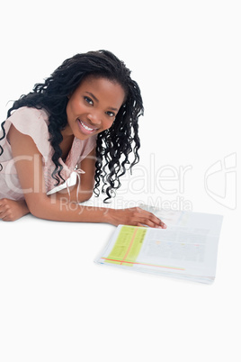 A smiling woman is lying on the floor with a book in front of he