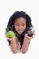 An apple and a bun are held up on the palms of a young womans ha