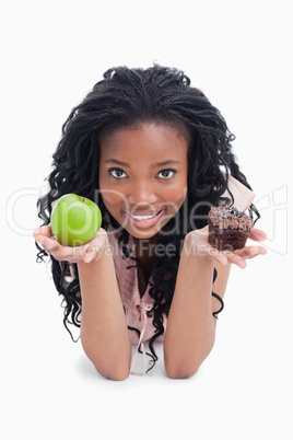 A young woman looking at the camera is holding an apple and a bu