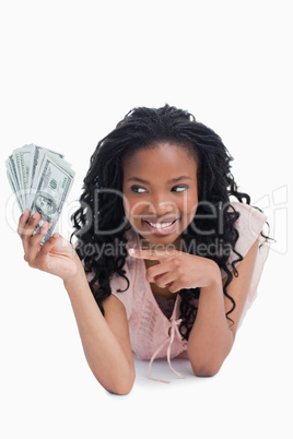 A smiling woman is pointing at American dollars in her hand