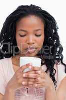 A young woman with her eyes closed is smelling coffee out of a c