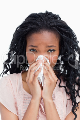 A young woman is blowing her nose in a tissue