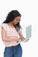 A happy young woman is typing on the laptop she is holding