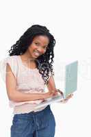 A young woman holding a laptop is smiling at the camera