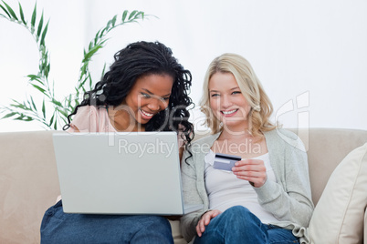 A woman holding a bank card is sitting with her friend who has a