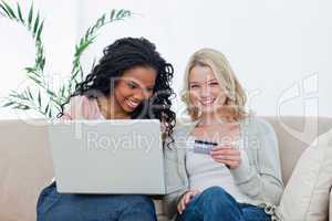 A woman holding a bank card is sitting with her friend who has a