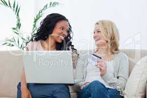 Two women looking at each other holding a bank card and a laptop