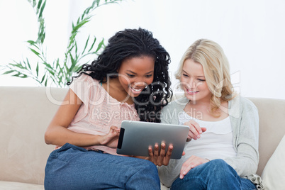 Two women sitting on a couch looking at a tablet computer