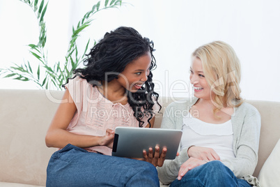 A woman holding a tablet computer is smiling at her friend