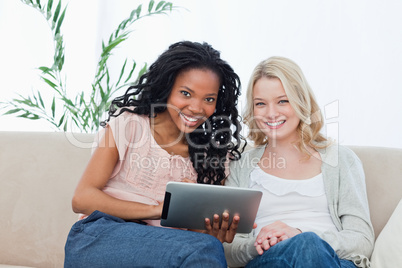 Two women smiling at the camera with a tablet computer in front