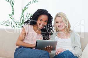 Two women smiling at the camera with a tablet computer in front