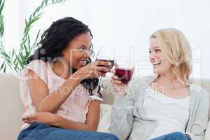 Two women holding wine glasses are smiling at each other