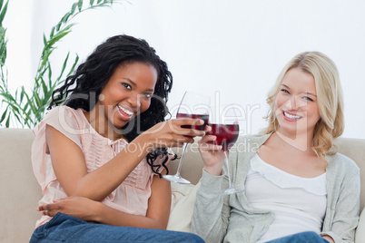 Two women holding wine glasses are smiling at the camera