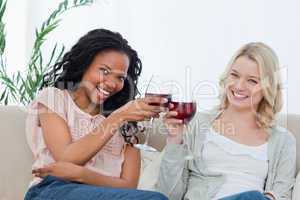 Two women holding wine glasses are smiling at the camera