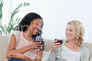 Two women sitting on a couch are holding wine glasses