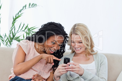 A surprised woman is pointing at a mobile phone that her friend