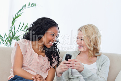 A woman holding a mobile phone is smiling at her friend