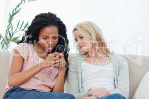 A woman is texting on her mobile phone while her friend watches