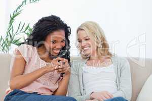 A woman holding a mobile phone is showing it to her friend
