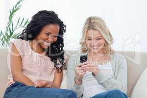 A woman holding a mobile phone is sitting on a couch with her fr