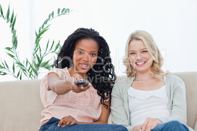 A woman with her friend is pointing a television remote control