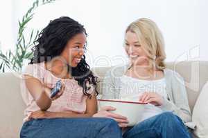 Woman holding a bowl of popcorn sitting longside a woman with a