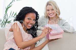 A woman holding a pink box smiles at the camera with her friend