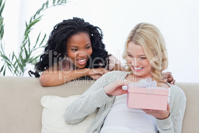 A smiling woman is holding a pink box and her friend is behind h