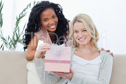 A woman holding a present is smiling at the camera with her frie