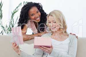 A woman opens a box containing a present and her friend smiles