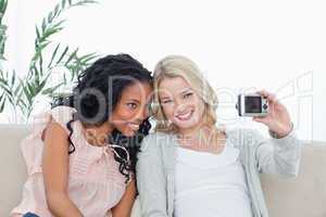 Two women are sitting down taking photo of themselves with a cam